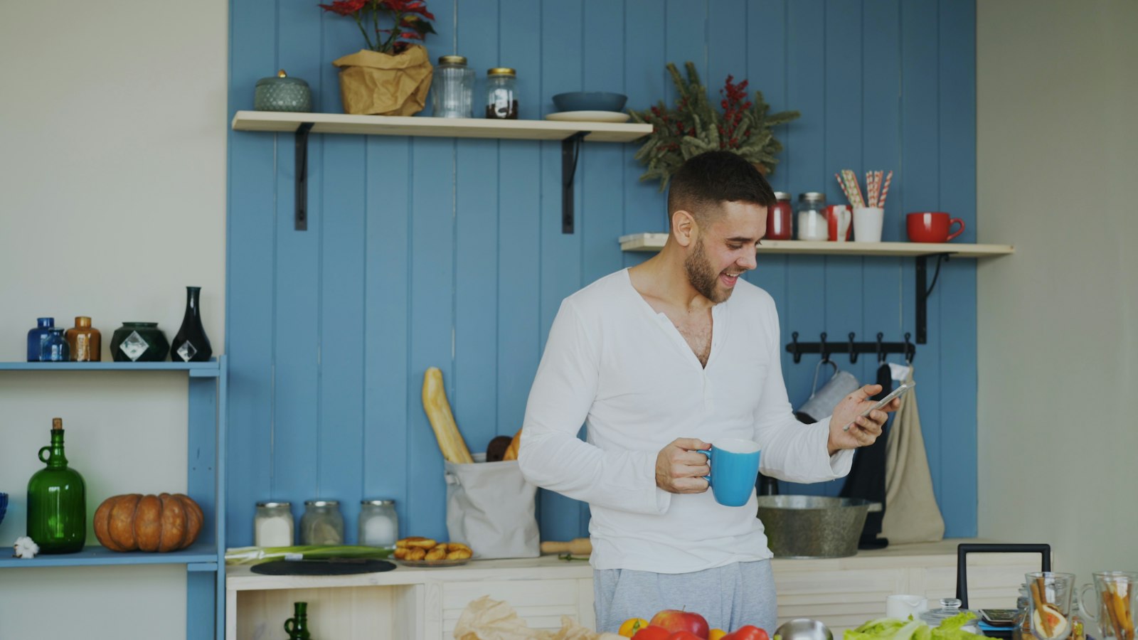 A man in a white shirt reading his phone in a bright kitchen