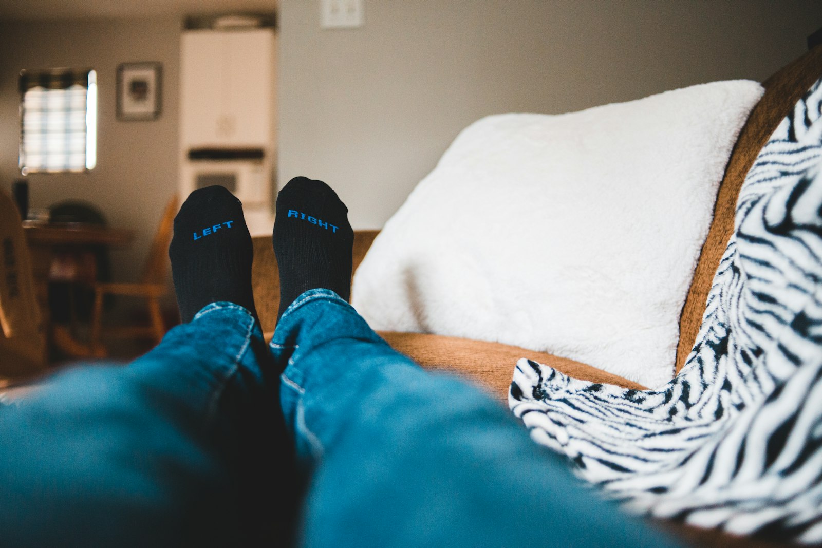 Feet in warm socks resting on a sofa beside a cushion